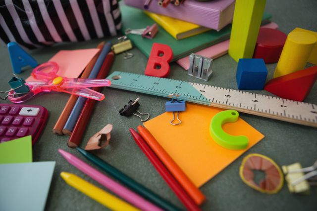 This image shows a variety of colorful school supplies scattered on a chalkboard. Items include pencils, a ruler, paper clips, erasers, and other stationery. Ideal for educational materials, back-to-school promotions, classroom decor, and organizational tips.