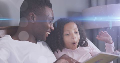 Father reading storybook to excited daughter in magical atmosphere