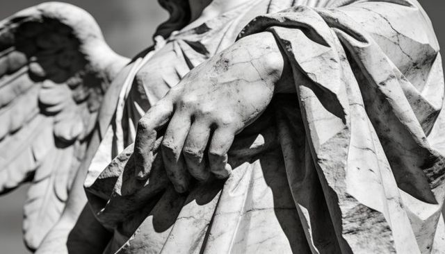 Weathered marble angel hand closeup showing drapery, veined texture, cracks at memorial