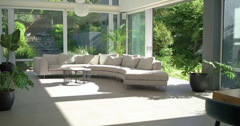 Sunlit curved sectional sofa in minimalist glass-walled living space with panoramic garden views
