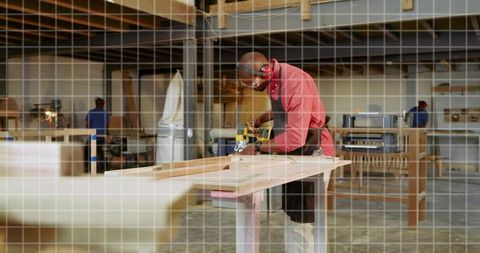 Carpenter sanding wooden plank with portable sander wearing goggles and apron in workshop