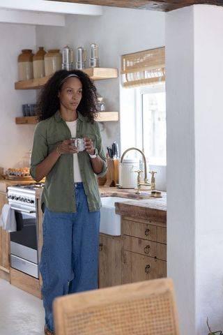 African american woman enjoying coffee in cozy rustic farmhouse kitchen with vintage sink