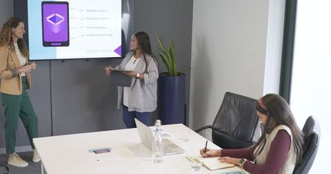 Diverse women presenting mobile app mockup in modern conference room