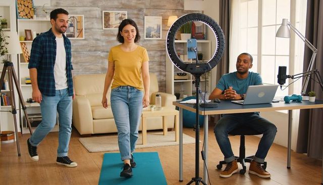 Creators filming home fitness walk: woman walking on mat with ring light and laptop