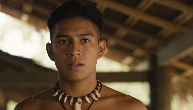 Young man wearing beaded tooth necklace under thatched roof rustic natural portrait