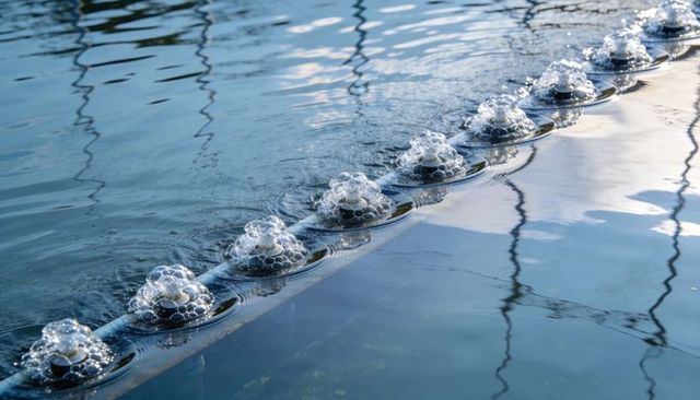 Diagonal row of domed bubbles releasing ripples across reflective blue water for aeration concept