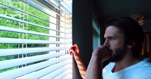 Man looking through window blinds after waking up at home 4k