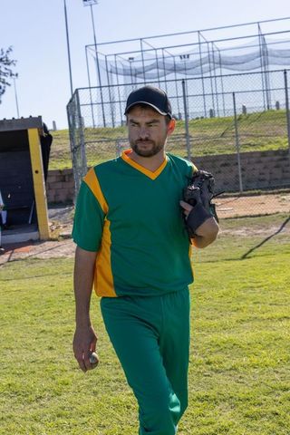 Baseball pitcher walking on field in green yellow uniform holding glove and ball