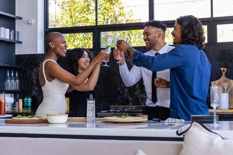 Diverse friends clinking champagne flutes at modern kitchen island during celebration