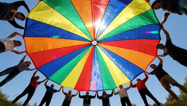 Holding giant rainbow parachute overhead, group demonstrating teamwork outdoors