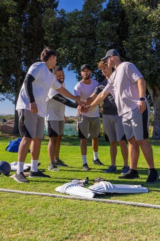 Diverse male athletes joining hands in outdoor huddle on park field promoting teamwork leadership