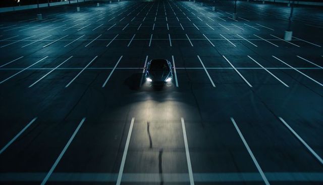 Lonely sedan illuminating empty parking lot at night with headlight beam and shadows