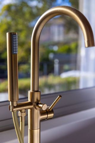 Brushed brass kitchen faucet with pull-out sprayer gleaming by window light modern luxury accent