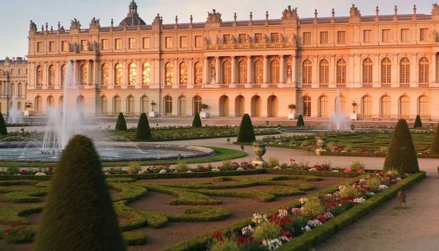 Sunlit neoclassical palace facade with formal parterre gardens and water fountains