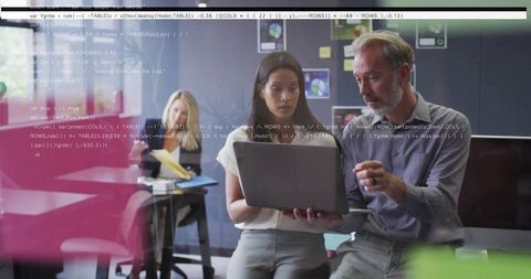 Colleagues reviewing code and strategy on laptop in glass boardroom for startup teamwork