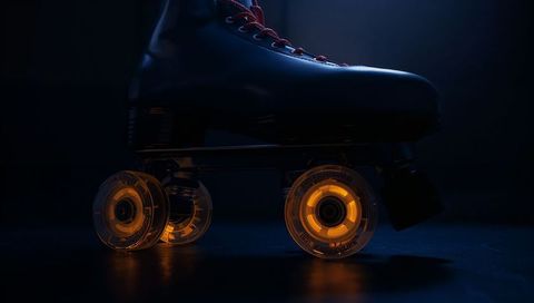 Resting black quad skate with glowing amber wheels and reflective blue studio lighting