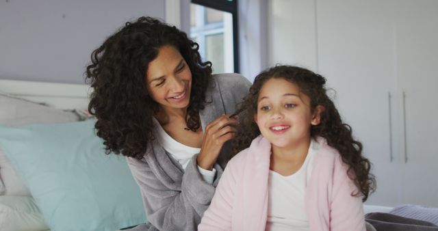 Happy biracial mother and daughter sitting in bedroom and playing with hairs. domestic life and leisure time concept.