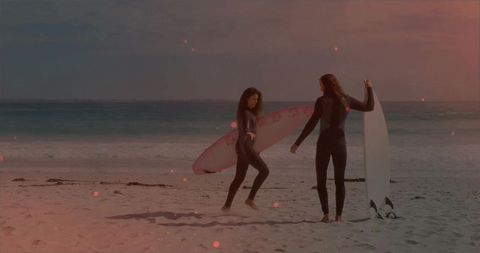 Women in Wetsuits with Surfboards on Sandy Beach at Sunset