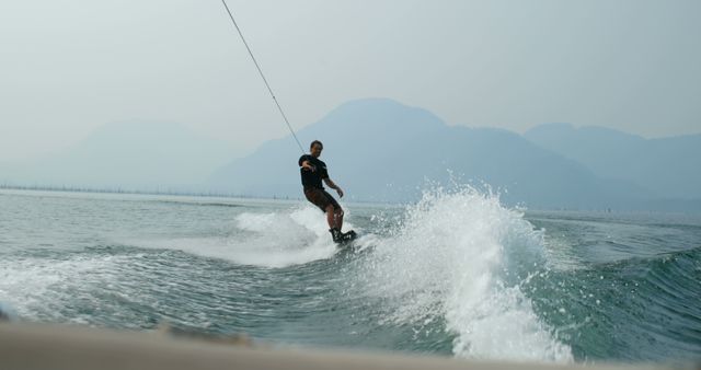 Man Wakeboarding on Lake with Misty Mountains in Background - Download Free Stock Images Pikwizard.com