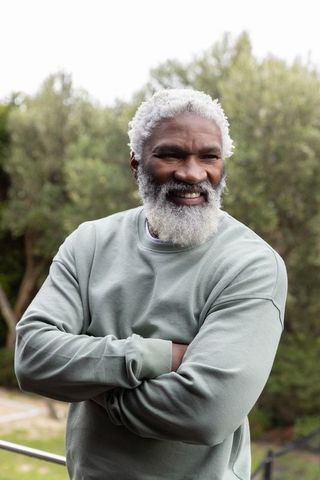 Senior african american man smiling with arms crossed on balcony wearing sage crewneck