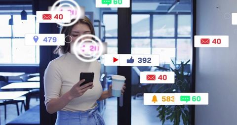 Asian woman checking smartphone notifications while holding coffee in modern office