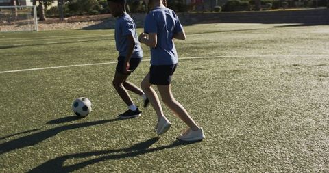 Teen soccer teammates dribbling on sunlit artificial turf during youth training session