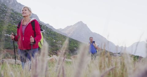 Senior Couple Hiking Through Mountain Landscape with Backpack and Poles
