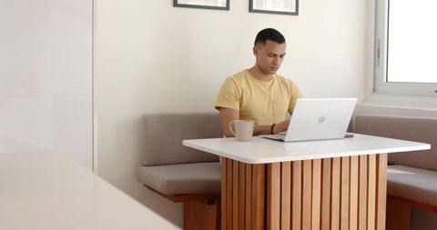 Young man working on laptop at modern dining nook for home office productivity and focus