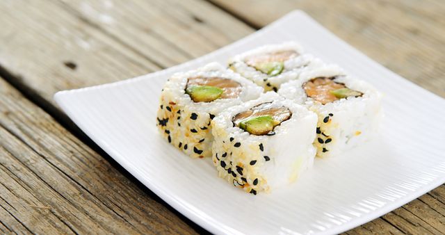 A plate of sushi rolls topped with sesame seeds is presented on a wooden table, with copy space. Sushi is a traditional Japanese dish that has gained worldwide popularity for its delicate flavors and artistic presentation.