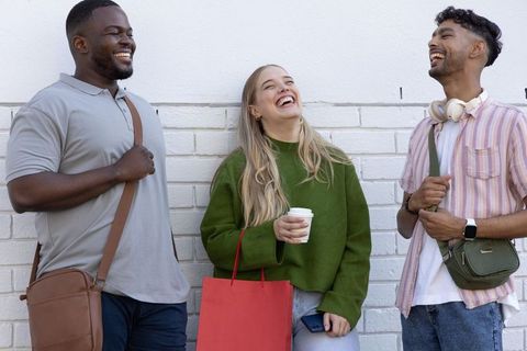 Laughing diverse friends chatting outdoors with coffee, shopping bags and headphones