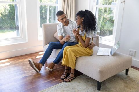 Young couple sharing tender moment on chaise lounge with laptop in bright living room