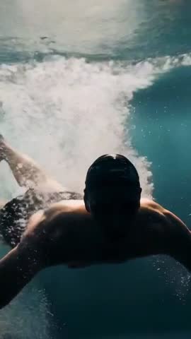 Underwater swimmer powering through pool with strong kick and bursting bubble wake