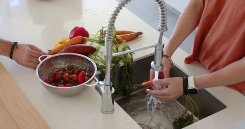 Couple washing fresh vegetables under modern spring-neck faucet preparing healthy meal