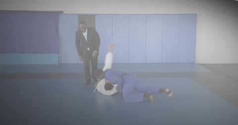 Judo throw training session with coach observing on mat in blue and white gis