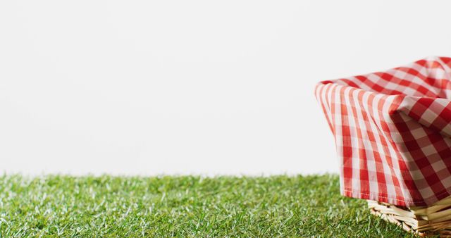 Picnic basket with checkered blanket on grass on white background with copy space. Picnic day, food and nature concept.