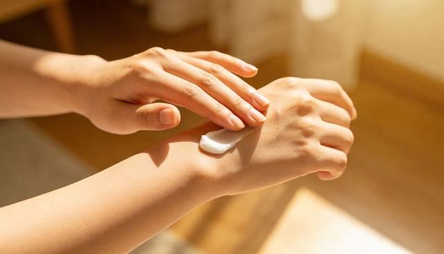Sunlit hands applying creamy moisturizer on back of hand closeup for skincare routine