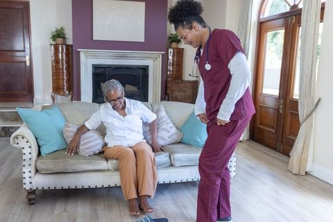 African american senior sitting on sofa receiving gentle home care from nurse smiling