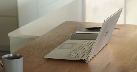 Minimalist home workspace featuring silver laptop, notebook and coffee mug on wooden desk