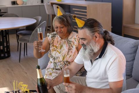 Senior couple celebrating birthday with champagne and cake in modern living room