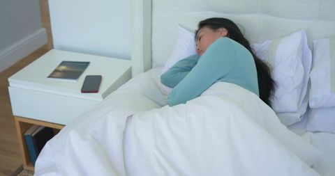 Mid-30s asian woman sleeping on side in bright minimalist bedroom with white duvet