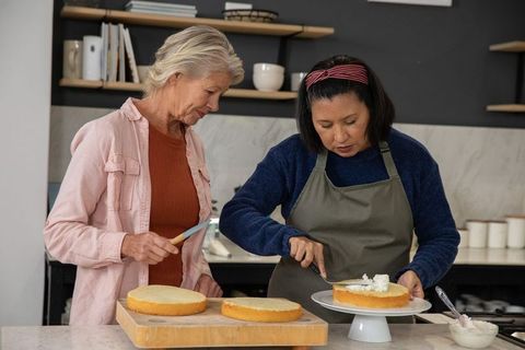 Senior women collaborating while frosting homemade layer cakes in modern kitchen