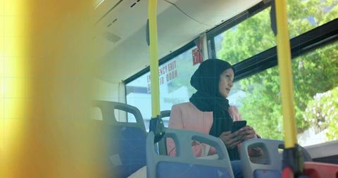 Woman in headscarf holding smartphone while traveling on city bus