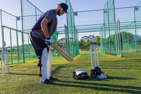Cricket batsman practicing in outdoor nets wearing pads and gloves on artificial turf
