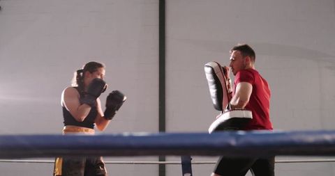 Female Boxer Sparring with Trainer Holding Focus Mitts in Boxing Ring