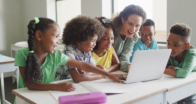 This image illustrates an engaging classroom scene with a diverse group of children learning with their teacher using a laptop. Ideal for educational content, multicultural learning materials, technology in education ads, and classroom environment articles.