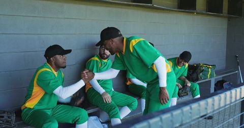 Baseball teammates shaking hands in dugout wearing green and yellow uniforms