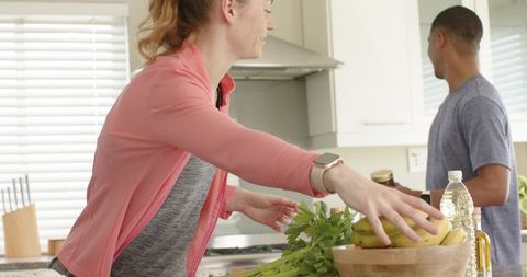 Couple preparing healthy meal in bright kitchen woman reaching for bananas man holding jar
