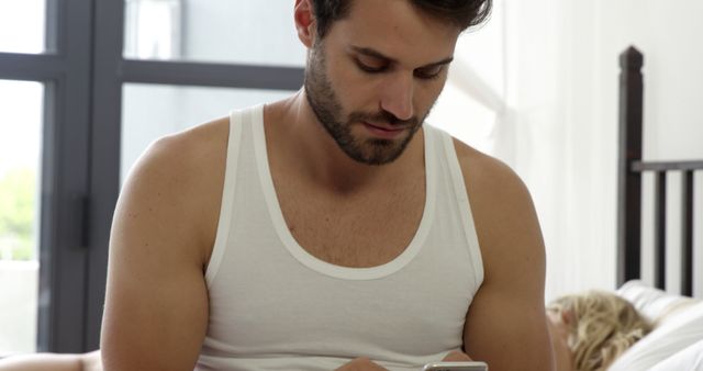 Man in White Tank Top Using Smartphone in Bedroom - Download Free Stock Images Pikwizard.com