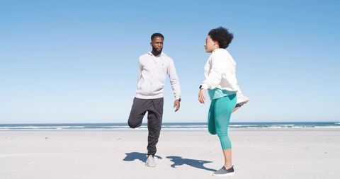African American Couple Stretching and Balancing on Sunny Beach Before Outdoor Workout