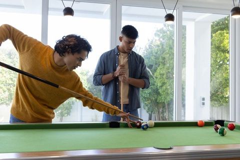 Young friends playing pool in modern home game room with green felt table and daylight